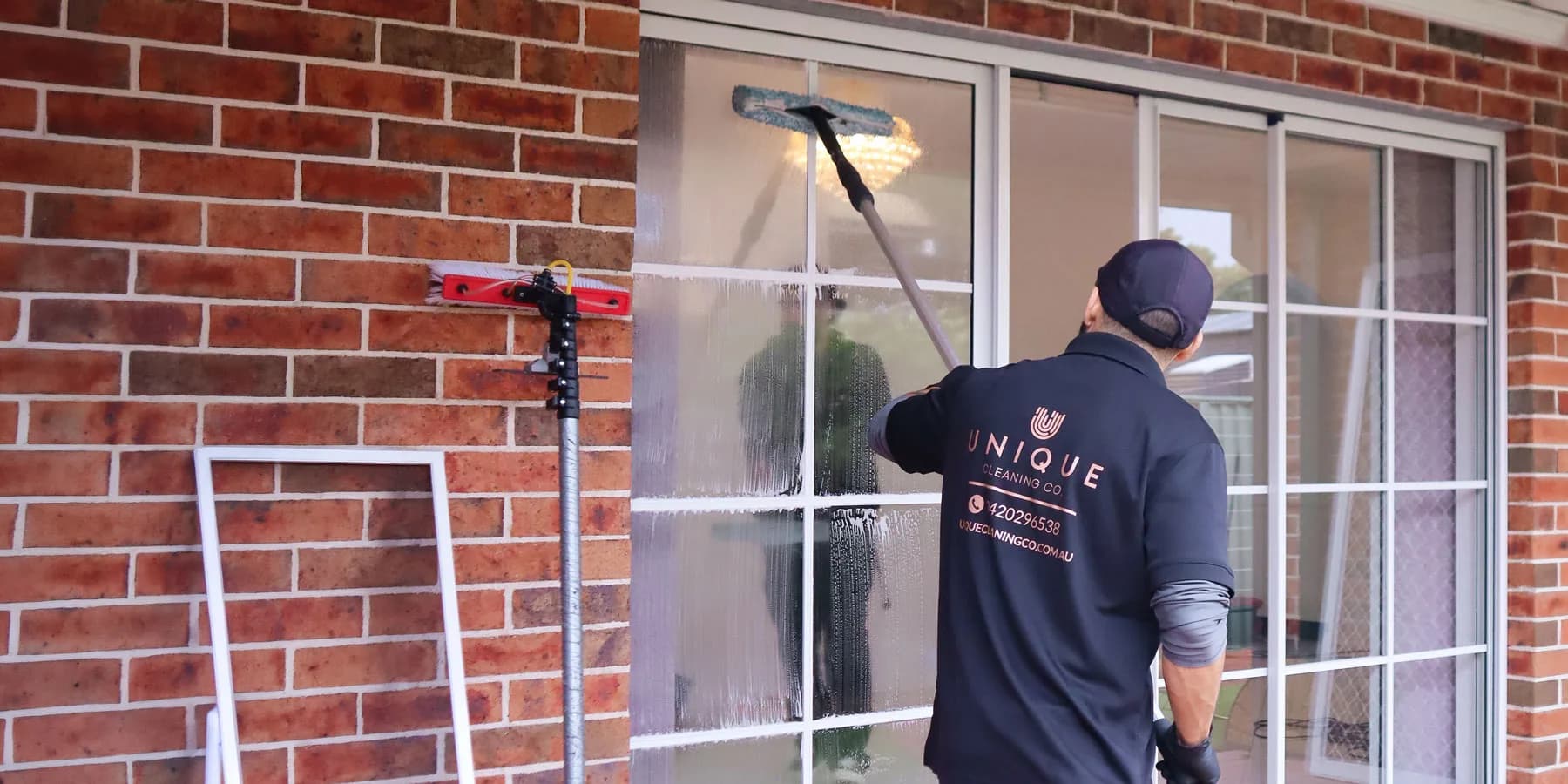 A Unique Business Co cleaner washing a home's sliding glass doors with a water-fed pole